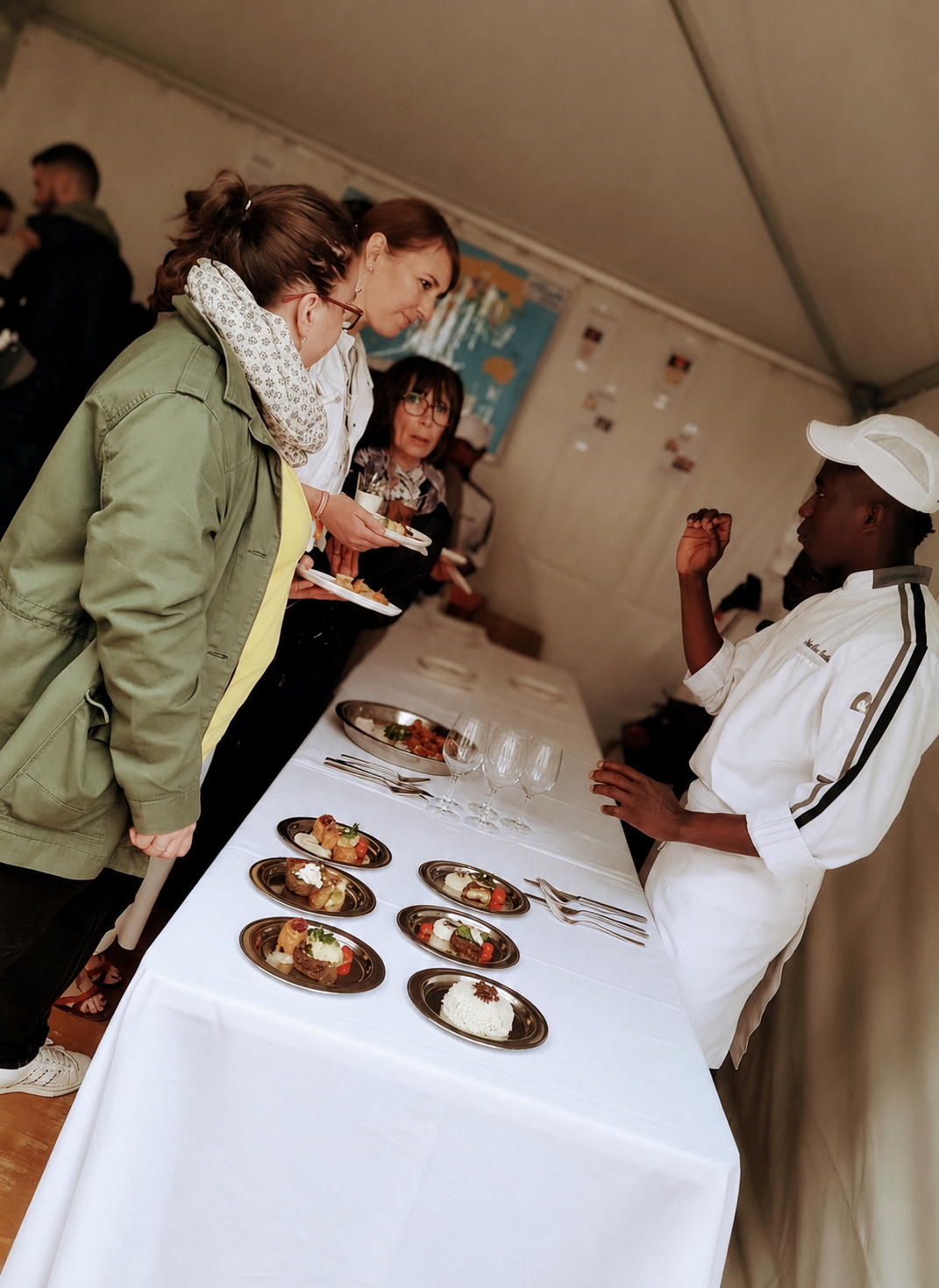 Chef en uniforme blanc présentant des créations dressées à des invitées autour d'une table