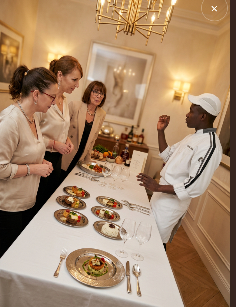 Chef en uniforme blanc présentant des créations dressées à des invitées dans un salon haussmannien